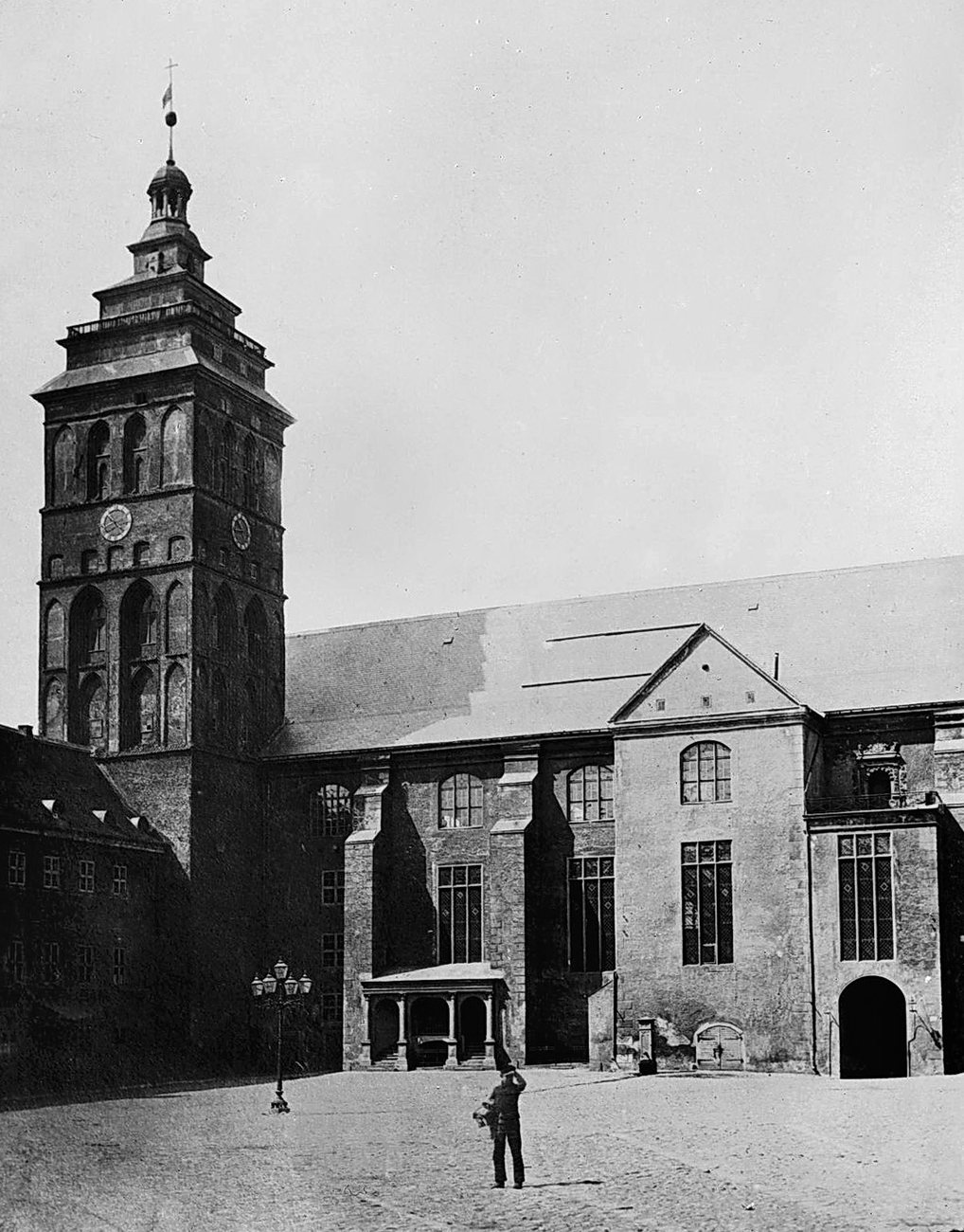 A lone man on the cobbles below the great tower and the west wing of Königsberg Castle in 1863