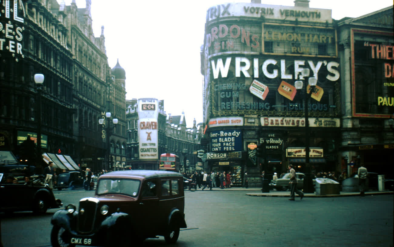 Advertising signs and a taxi at the corner of Shaftesbury Avenue and Piccadilly Circus, London, in the early 1950s