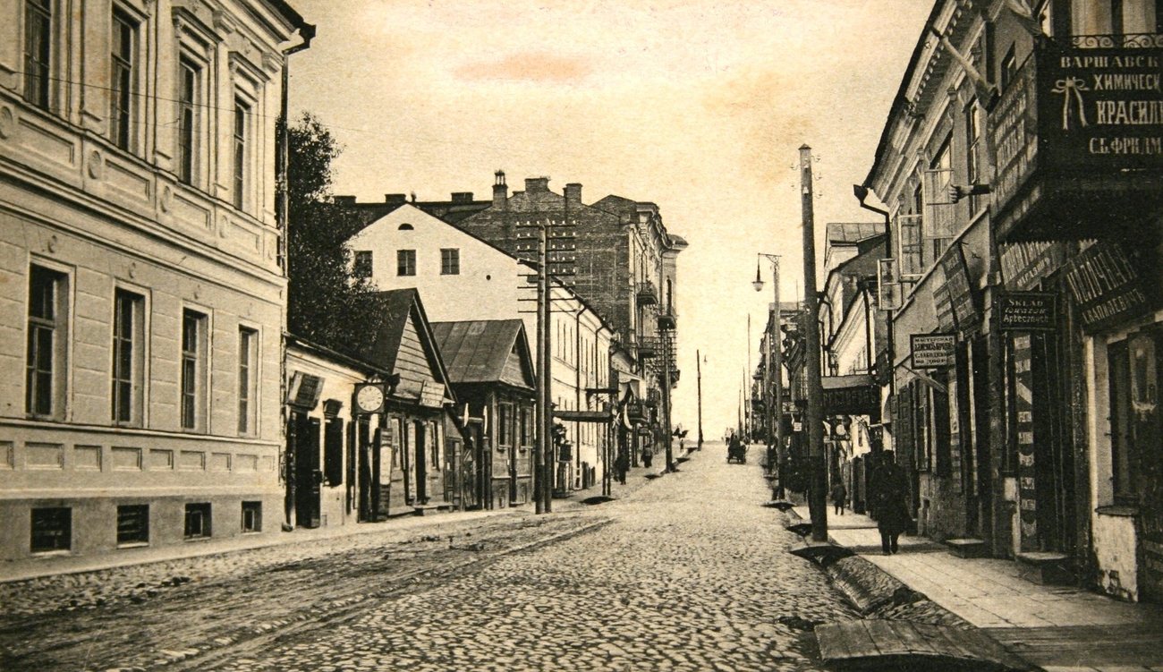 Shop signs over the pavements of Petropavlovskaya Street in Minsk around 1910, the cobbled street running between low houses and taller blocks