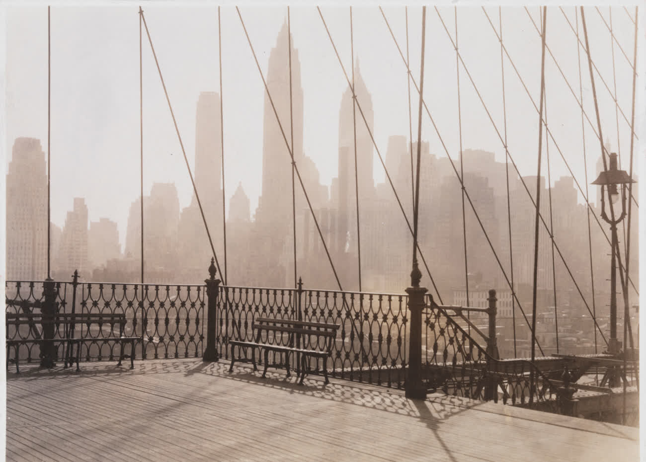 The Manhattan skyline in haze, seen through the cables of the Brooklyn Bridge walkway in 1950
