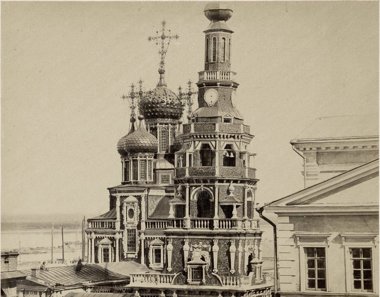 The carved domes and clock-faced bell tower of the Stroganov Church in Nizhny Novgorod in 1861, with the river and moored boats behind
