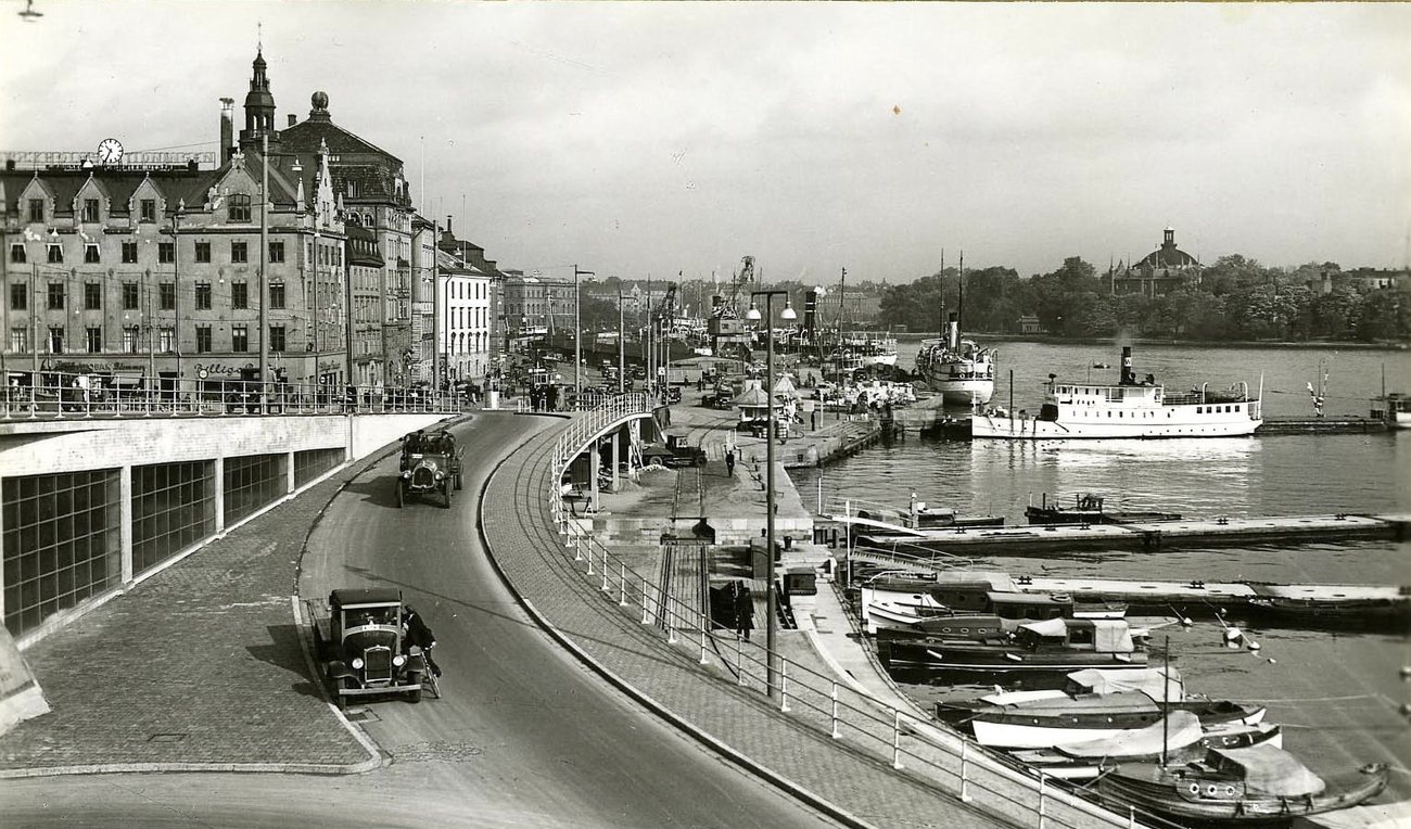 Cars on the curving ramp at Slussen in Stockholm in 1930, with white steamers and motor launches moored along the Skeppsbron quay