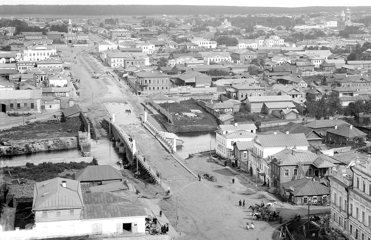 A high view east along Pokrovsky Prospekt in Yekaterinburg in 1885, over a river bridge, carts and low rooftops to church towers on the horizon