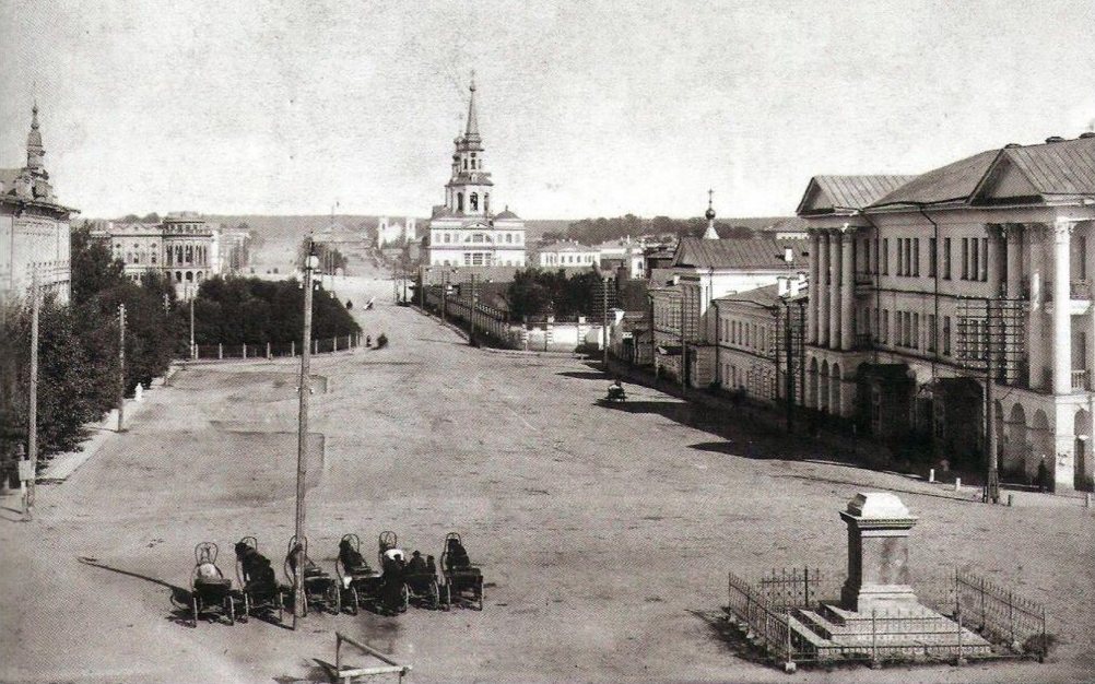 A row of horse cabs waiting on the broad Cathedral Square in Yekaterinburg in the early 1900s, a church spire closing the view down the street